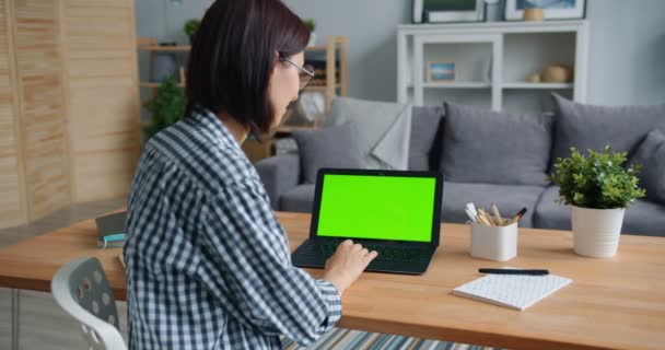 Ragazza sorridente utilizzando il computer portatile con schermo verde che lavora con il computer a casa — Video Stock