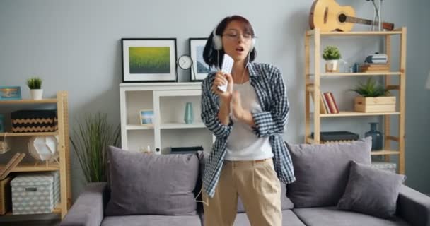 Chica juguetona cantando en control remoto bailando escuchando música en auriculares — Vídeo de stock