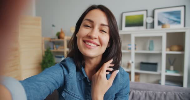 Взгляд девушки, делающей селфи улыбающейся, позирующей перед камерой дома — стоковое видео