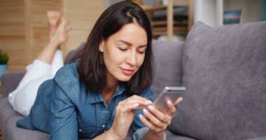 Evde rahatlatıcı akıllı telefon touchign ekran tutan çekici genç kadın