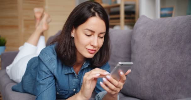 Aantrekkelijke jonge vrouw Holding smartphone touchign scherm ontspannen thuis — Stockvideo