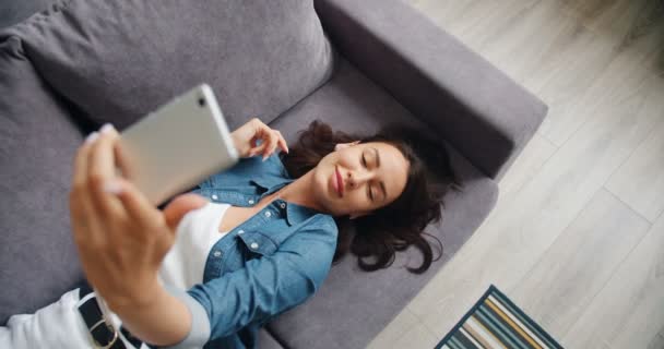 Вид зверху красива молода леді бере селфі зі смартфоном, що лежить на дивані — стокове відео