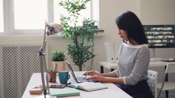 Young woman working with laptop when assistant brigning her pile of documents — ストック動画