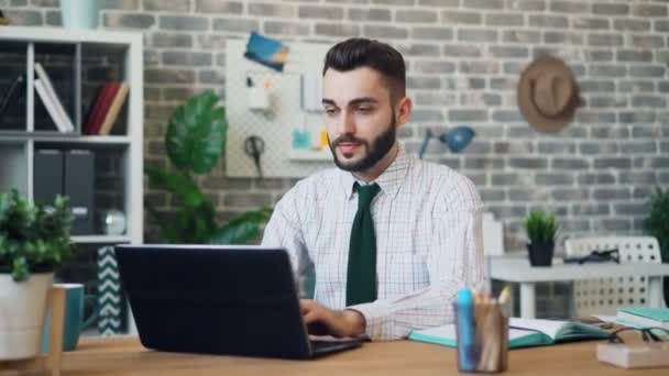 Portret van de jonge man werken met laptop dan kijken naar camera glimlachend — Stockvideo