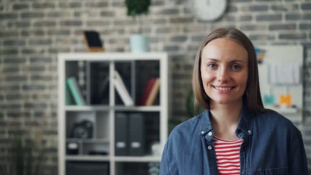 Ritratto di giovane donna gioiosa che sorride guardando la macchina fotografica in piedi sul posto di lavoro — Video Stock