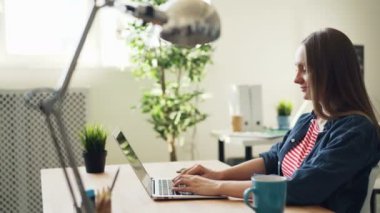 Gülümseyen ofis çalışanı, masa başında çalışmanın keyfini çıkarırken modern dizüstü bilgisayar kullanarak yazarak