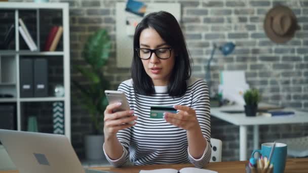 Девушка, платящая онлайн с помощью кредитной карты с помощью смартфона на рабочем месте — стоковое видео