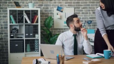 Genç adam dizüstü bilgisayarla çalışıyor sonra da ofiste güzel bir kadınla konuşuyor.