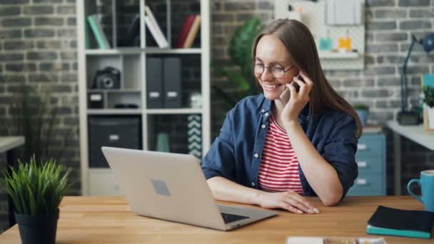 Gyönyörű nő használ laptopot és beszél a mobiltelefonon a munkahelyen — Stock videók