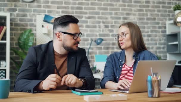 Male and female coworkers discussing work sitting at desk with laptop together — Stock Video