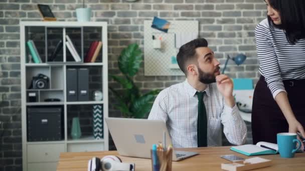 Jeune homme travaillant avec un ordinateur portable puis parlant à une collègue jolie femme au bureau — Video