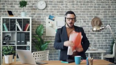Dikkatsiz ofis çalışanı müzik atma kağıtları ve not defteri dinlerken dans