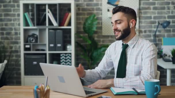 Joyful office worker making video call with laptop wireless earphones at work — Stock Video