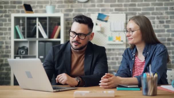 Mann und Frau schauen auf Laptop-Bildschirm und unterhalten sich während des Arbeitstages im Büro — Stockvideo