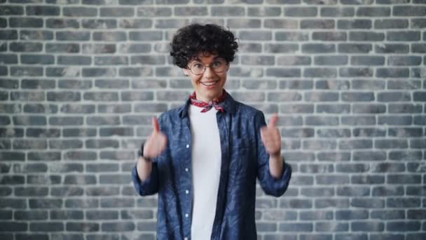 Portret szczęśliwej Brunetki w okularach pokazując kciuki na tle cegły — Wideo stockowe