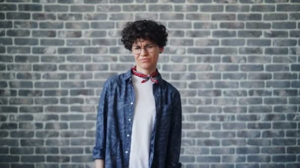 Portrait of disappointed girl showing thumbs-down on brick background — Stock Video