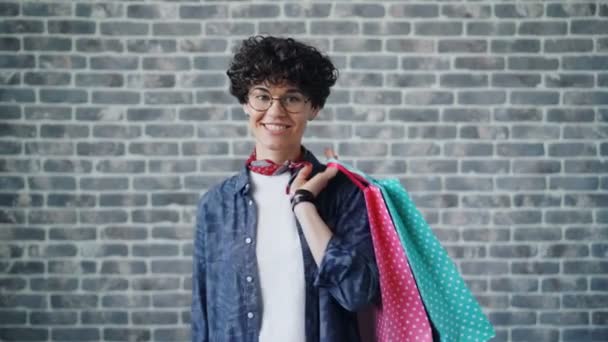 Портрет радостной девушки-шопоголика, держащей сумки с покупками, смотрящей в камеру — стоковое видео