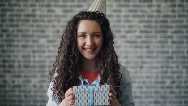 Portret van schattig meisje in feest hoed aanbod geschenk doos glimlachend kijken naar camera — Stockvideo