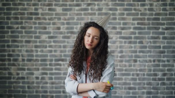 Porträt einer unglücklichen jungen Frau, die mit traurigem Gesicht in der Nähe einer Mauer in das Partyhorn bläst — Stockvideo