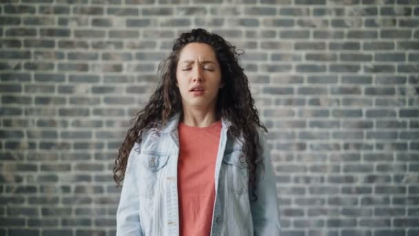 Retrato de mujer joven enferma estornudando mirando a la cámara en el fondo de la pared de ladrillo — Vídeos de Stock