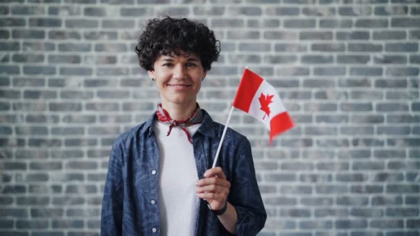 Retrato em câmera lenta de estudante bonito segurando bandeira canadense no fundo de tijolo — Vídeo de Stock