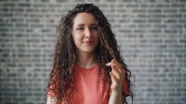 Retrato de mujer linda enrollando el pelo alrededor de dedo coqueteando mirando a la cámara — Vídeos de Stock