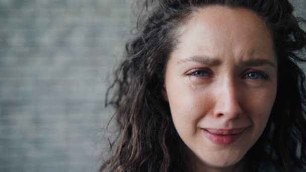 Retrato de cerca de una joven infeliz llorando sobre un fondo de pared de ladrillo — Vídeos de Stock