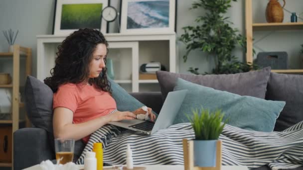 Хіба молода леді, використовуючи ноутбук, що переглядає кашель на дивані, торкається бігового носа — стокове відео