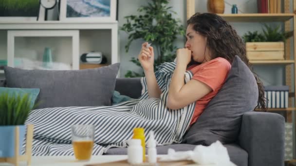 Zijaanzicht van de jonge vrouw het nemen van temperatuur met thermometer in huis op de Bank — Stockvideo