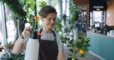 Güzel bayan çiçekçi fıskiye gülümseyerek tutarak tencerede egzotik bitki sulama