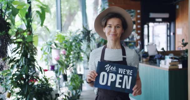 Çiçekçi dükkanı sahibinin portresi biz işyerinde ayakta açık işareti tutuyor — Stok video