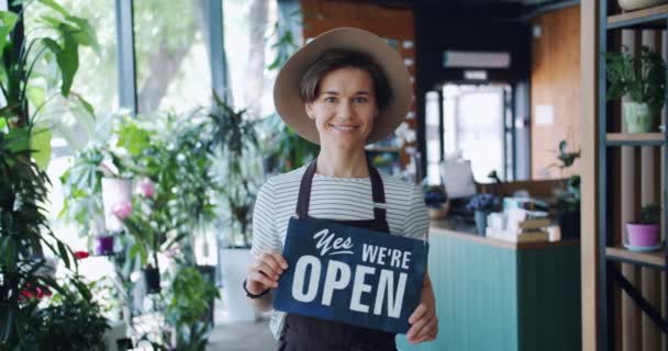 Retrato de chica encantadora sosteniendo sí estamos abiertos signo de bienvenida a la tienda de flores — Vídeo de stock