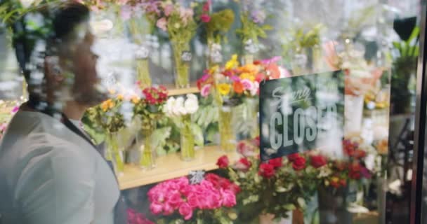 Mouvement lent du propriétaire d'entreprise portant nous sommes signe ouvert sur la porte de magasin de fleurs — Video