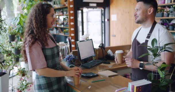 Pokladník v květinářství mluví s obchodníkem, aby šla na kafe s úsměvem. — Stock video