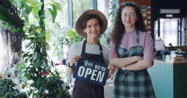 Медленное движение красивых женщин холдинг мы открыты знак стоя в цветочном магазине — стоковое видео