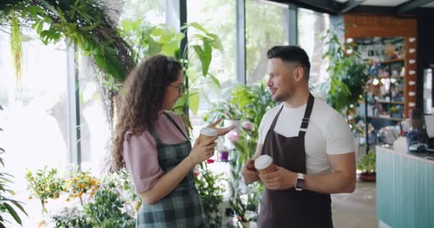 Man en vrouw bloemisten praten houden om koffie te gaan tijdens het breken in bloemenwinkel — Stockvideo