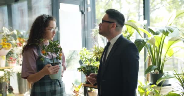 Florist Pretty Girl säljer exotiska växt till medelålders man i blomsteraffär — Stockvideo