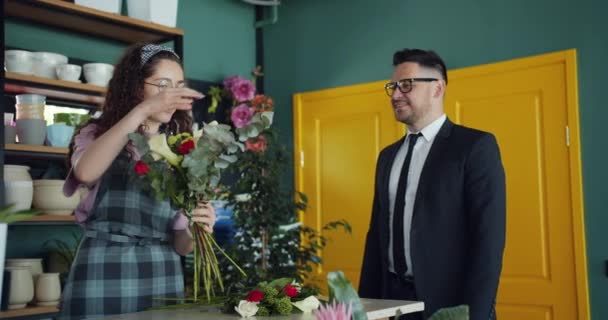 Přátelský květinář, který zařizuje květiny a hovoří se zákazníkem v obchodě — Stock video