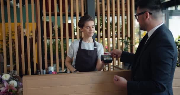 Vriendelijke bloemist die bloemen verkoopt aan Guy terwijl de klant betaalt met een creditcard — Stockvideo