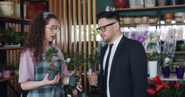 Neşeli insanlar çiçekçi ve müşteri çiçek deposunda yeşil bitkiler tartışıyor — Stok video