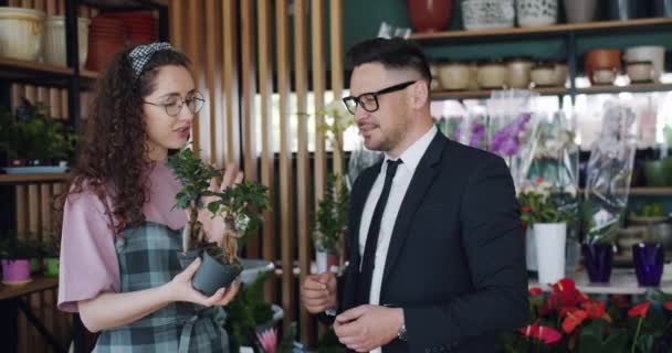 Söt florist beskriver vackra gröna växter till skäggiga man i Flowers Shop — Stockvideo