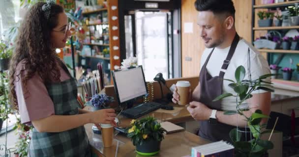 Slow motion of flower store employees talking discussing plant holding coffee — Stock Video