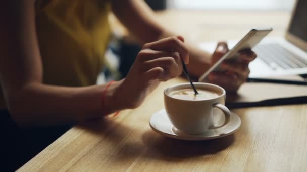 女性手将咖啡混合在杯子中，在咖啡馆使用智能手机放松的特写镜头 — 图库视频影像