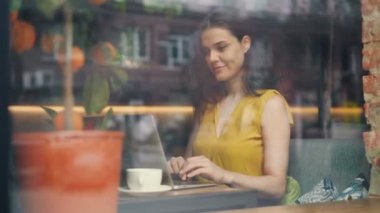 Kafede dizüstü bilgisayarla çalışan genç kadın masada gülümseyerek yazarak