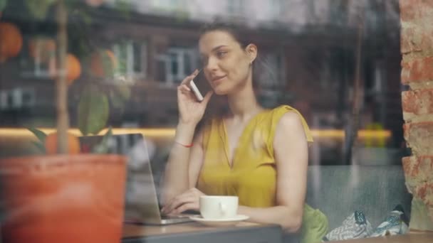 Радостная деловая женщина разговаривает по мобильному телефону и пользуется ноутбуком в кафетерии — стоковое видео