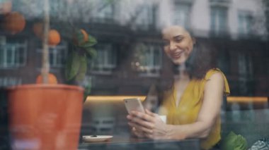 Kafede güzel bir gün boyunca akıllı telefon ekranına bakan gülümseyen genç kadın