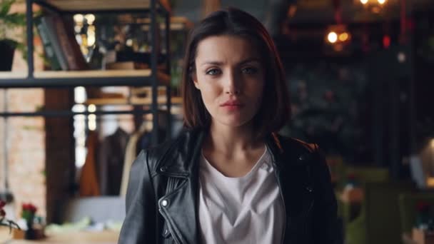 Portrait of beautiful young lady in leather jacket in cafe with serious face — Stock Video