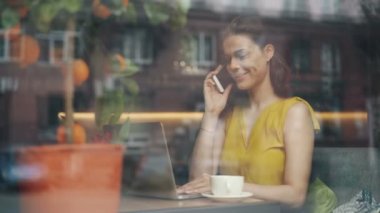 Kız cep telefonu konuşuyor ve öğle yemeği molası sırasında kafede oturan dizüstü bilgisayar kullanarak