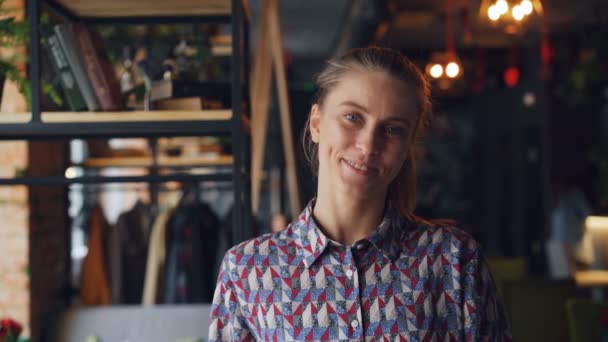 Портрет милой молодой девушки-студентки в уютном кафе, улыбающейся, глядя в камеру — стоковое видео