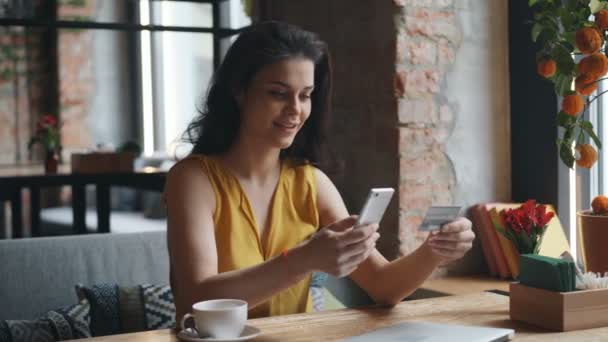 Jovem mulher fazendo pagamento online com smartphone no café segurando cartão bancário — Vídeo de Stock